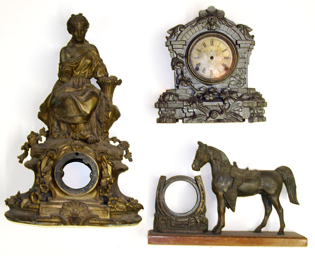Three cast-metal clock cases (no movements). Horse and lucky horseshoe figural has wooden base. Silvery finish is a cast front with wood movement box. Best is very large figural of seated lady, 22" tall. — Antique Clocks Price Guide