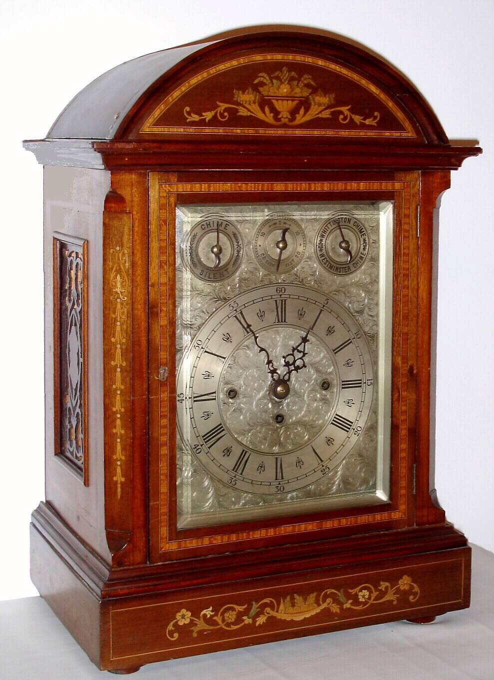 English, large inlaid mahogany quarter chiming bracket clock, 3-fusee, chiming on your choice of 8 bells or 4 gongs [and striking the hours on a deep toned cathedral gong, with a rectangular dial, engraved and silvered, and with subsidiary dials in the arch for Chime / Silent, F /S , and Whittington or Westminster tune, serviced by B. G. Taylor, Marple (Stockport), label on rear of dial. The case with wooden side frets, bun feet, and floral inlay on the canted corner moldings and front panels, + cross banding around the door, sides and top. C.1885. — Antique Clocks Price Guide