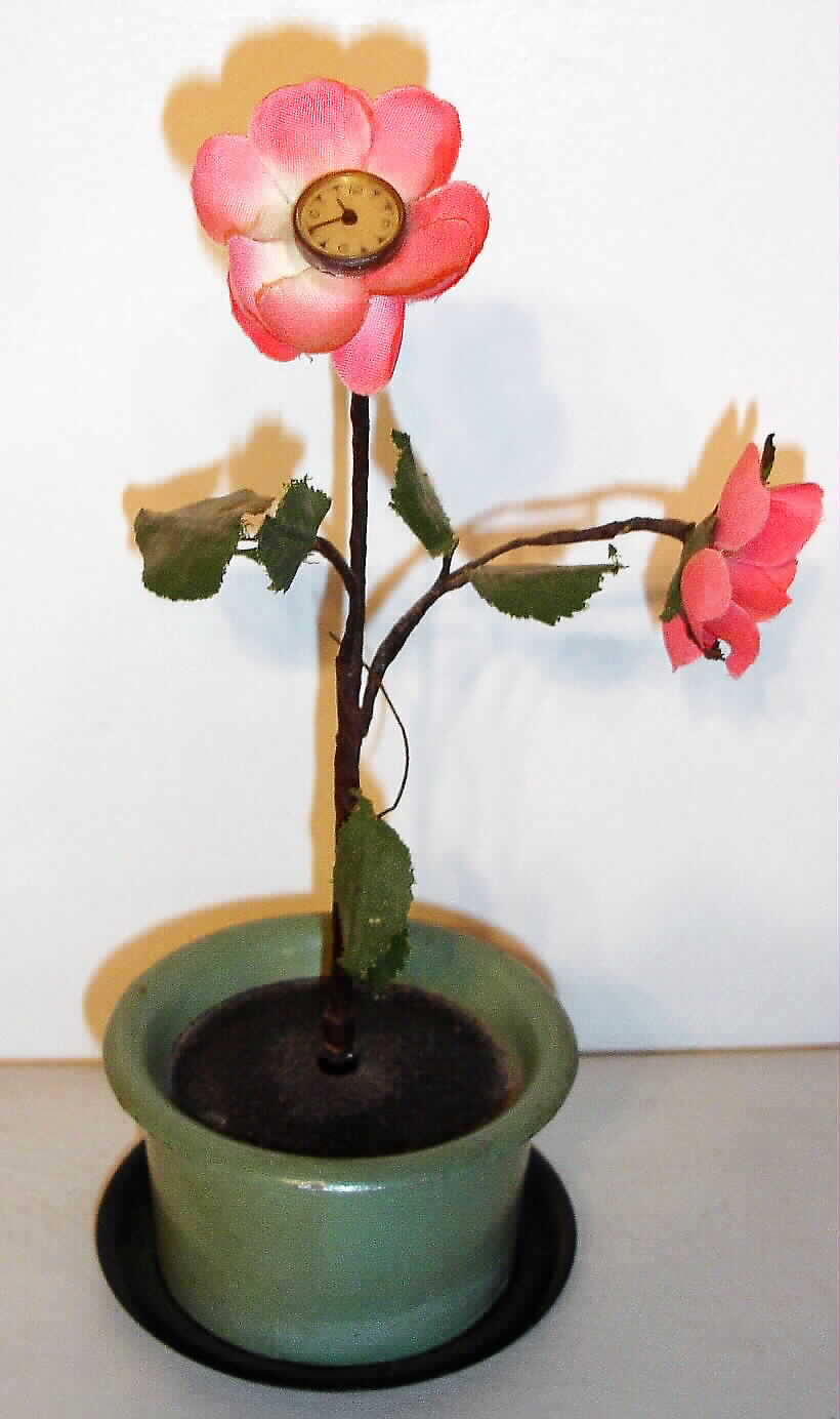 Desk clock German two rose plant with fabric petals and leaves in painted cast metal pot with Arabic numeral dial inset into center of upper rose, stem wind and stem set movement concealed in pot, c1930 — Antique Clocks Price Guide