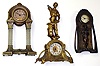 Three large cast metal American novelty clocks. Rear wind pin pallet movements. Shortest Nouveau style is a New Haven. Middle has nice square glass columns. Tallest, in gold finish, of blacksmith (missing arm) is 18" high.
