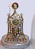English, Single Fusee skeleton clock with anchor escapement and single passing strike at the hour, the frame resting on 8 cast round feet mounted to a gray marble base, with a 2" plexi-glass spacer added to allow the old glass dome to clear the clock and hammer when striking.