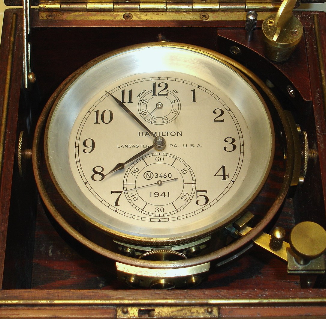 Hamilton Watch Co., Lancaster, PA, Model 21 marine chronometer with 56 hour up/down indicator, 85 size,14J, key wind, chain fusee driven damascene nickel movement with spring detent escapement, giant uncut AMAC solid monometallic weighted chronometer balance, free sprung Elinvar class helical hairspring system and balance lock for hacking or shipping located next to winding hole, operated by allen wrench (included) The silvered 4 1/8" Arabic numeral dial is engraved "HAMILTON LANCASTER PA., U.S.A. N3460 1941" and has blacked steel hands, s#2E3460. The lot includes the original gimbaled inner dark red mahogany stained box with full brass banding, corners, handles and central tongue in groove seal with Hamilton tag, original key and setting instructions — Antique Clocks Price Guide