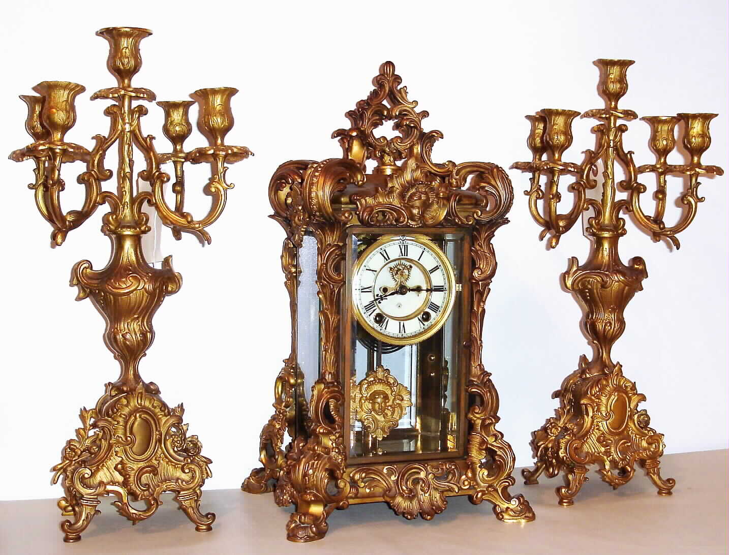 Ansonia Clock Co., New York, "Apex" crystal regulator three piece garniture set with matching candelabra 8 day, time and gong strike spring driven movement in gilded brass case with four beveled glasses and Roman numeral cream enamel dial, c1905 — Antique Clocks Price Guide