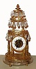 French mantel clock, 8 day, time only, spring driven, verge fusee movement and balance wheel in a three tiered gilded brass pillared case with canopy top resting on a rock crystal with four gilded feet. Tear drop rock crystal prisms are suspended from the three tiers. The white enamel chapter ring exposes the skeletonized movement, c1860