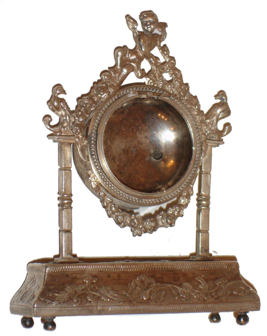 Continental desk or bedside clock case, purpose made to contain the inner case and movement of an earlier pair cased watch, bombe base on ball feet with square columns supporting the round case, with cast floral swag and putti, the top of each column with an inward facing bird, the base and clock case surfaces decorated with repousse ornament in the rococo style, beaded bezel surround, the back with hinged door bearing a silver standard mark, possibly French, right front foot also with a small letter mark, c1850 — Antique Clocks Price Guide