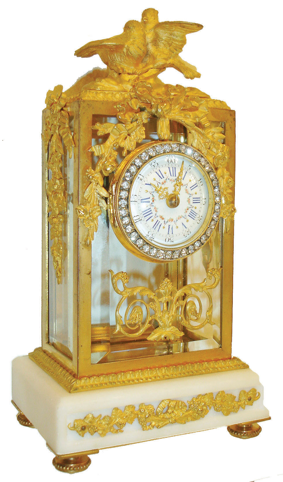 France, desk or table clock, case with gilt brass frame set with beveled glasses, rear door with plain glass, the top with gilt birds, case front and sides with bowknot suspended floral garlands, classically inspired scrolled foliate element below dial, on a white marble base with inset grape and leaf ornament, on beaded toupie feet, brilliant set bezel with convex beveled glass, Roman numeral white enamel dial with Arabic black outer 5 minute markers, and with polychrome floral swag decoration, gilt Louis XV style hands, small 8 day time only movement with cylinder platform, c1910 — Antique Clocks Price Guide