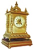 France, gilt brass mantel clock, on turned feet, deep cavetto base with modified egg and dart design, the four corners with ornately turned columns, the top with 5 finials and squat dome with bead molding, gilt bezel with beveled glass, Arabic numeral white enamel dial, blued steel hands, 8 day time and strike pendule a Paris movement signed S. Marti, striking on a gong, all on a gilt, molded wooden base on compressed ball feet, c1900