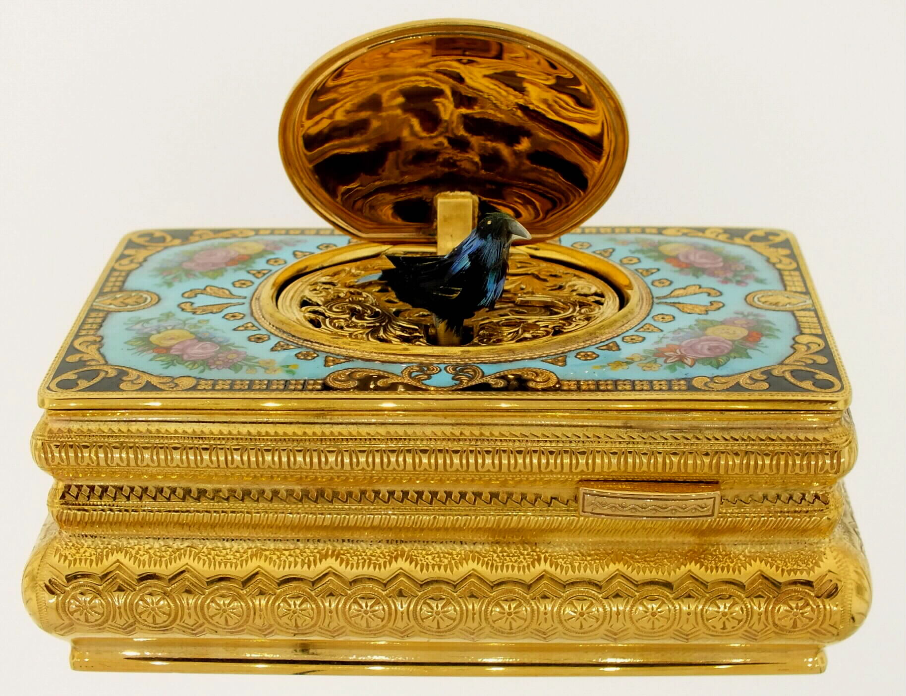 Swiss bird box with heavily patterned gilt brass case, top with bright cut engraved ornament, decorated in colorful enamels, the lid with a scene of nude bathers in a rural landscape, the bird with green, black, and blue feathers.  Late 20th century — Antique Clocks Price Guide