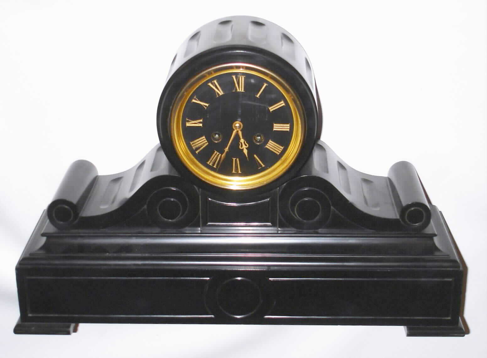 Tiffany and Co., New York, French black slate Drumhead style mantel clock, spring powered eight day time and strike movement signed Tiffany and Comp., striking the hours and half hours on a bell, fluted cylindrical case supported by scrolls on a molded rectangular base, decorated with shallow carving, the scrolls with volutes, gilt bezel with beveled glass, black slate dial with engraved Roman numerals finished with gold, polished brass hands, c1880 — Antique Clocks Price Guide