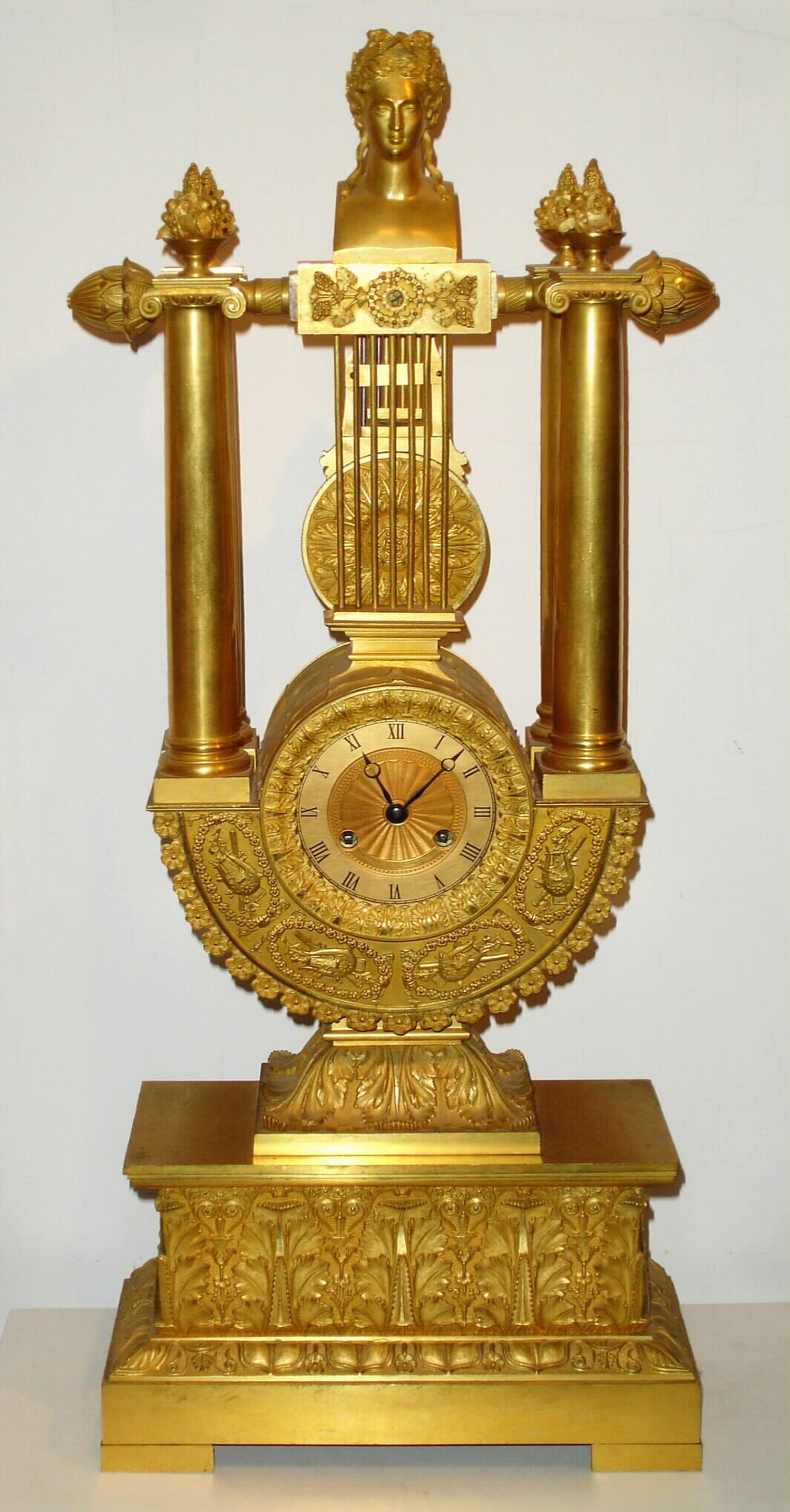 French, Empire style lyre mantel clock, with knife edge suspension of pendulum above the dial, 8 day spring driven movement numbered 210. The case profusely decorated with acanthus leaves, pineapples to the right and left of the top, and each column surmounted by a small urn with floral display, c1830 — Antique Clocks Price Guide