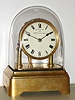 Eureka Clock Co, London, "1000 Day Electric Clock, electro mechanical mantel clock, battery powered, time only with large cut bimetallic balance and blued steel balance spring, Roman numeral white enamel dial with heavy gilt bezel, blued steel hands, movement with spotted back plate, supported on gilt columns, with finial style nuts securing the movement, all on a gilt brass base, and covered with a glass dome, s#14614 c1910