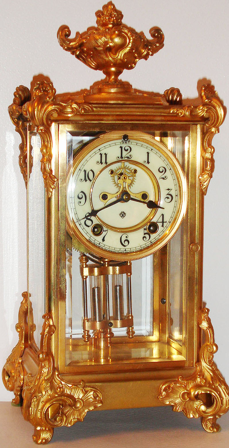 Ansonia Clock Co., New York, NY, "Marquis" model crystal regulator, eight day time and strike movement, open escapement, simulated mercury pendulum,  white enamel Arabic numeral dial, blued steel hands, gilt brass case with gilt spelter ornament, beveled glass panels c1900 — Antique Clocks Price Guide
