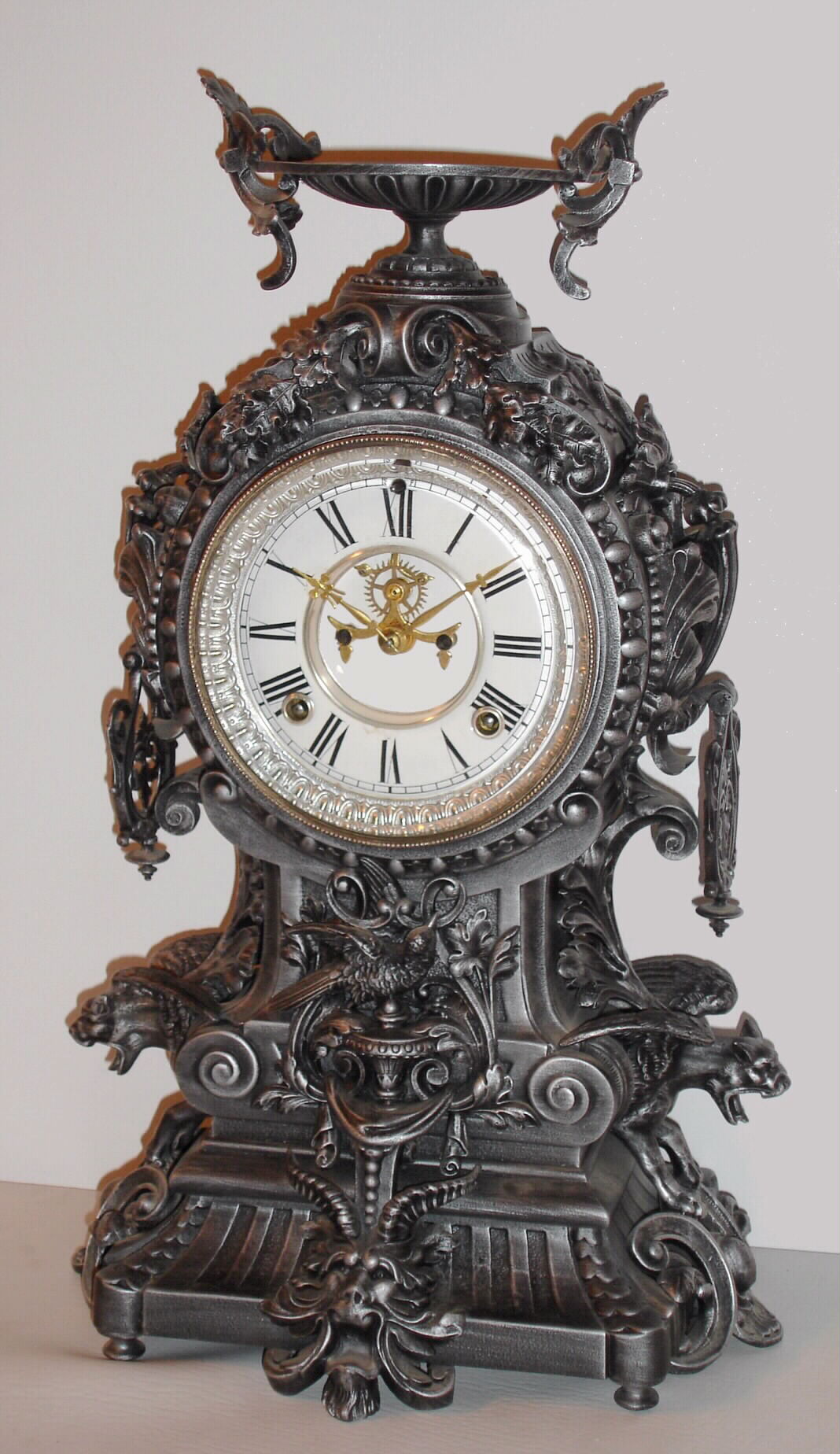 Ansonia Clock Co., New York, NY, "FRANCONIA", cast metal fantasy clock, featuring flying gargoyles to the sides, a bird below the dial and profuse scrolls and swirls, surmounted by a winged urn, c1894. — Antique Clocks Price Guide