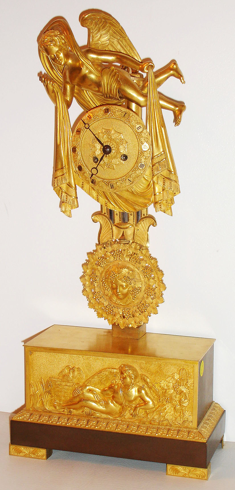 French mantel clock, 8 day, time and strike, pendule a Paris movement, with recoil escapement and count wheel, signed "Chappe a Paris", the gilt bronze case with winged figure, holding drapes on either side of the gilt Roman numeral dial with grape and leaf ornament, blued steel Breguet style hands, simulated gridiron pendulum in gilt bronze and polished steel, pendulum also with grapes and leaves theme surrounding a female bust, the base with reclining winged figure, a pair of doves, and more grapes, on a red patinated plinth supported by palm decorated gilt feet, c1825, — Antique Clocks Price Guide