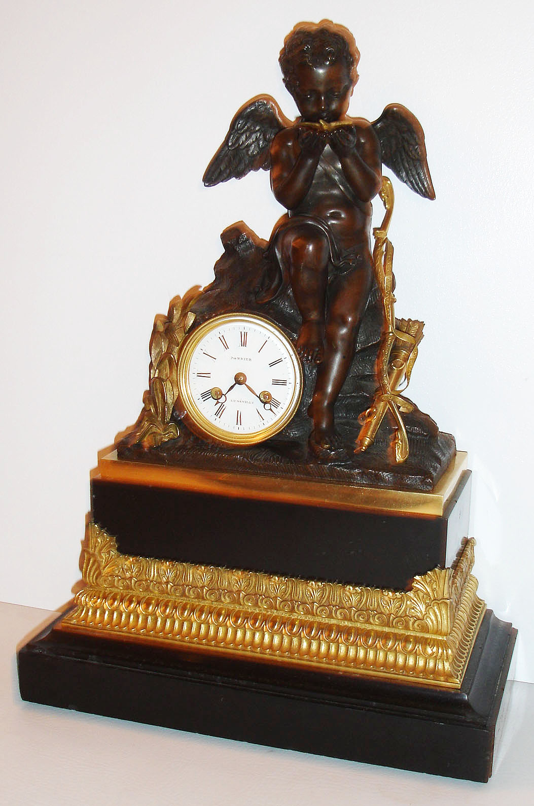 French mantel clock, gilt and patinated bronze and polished black slate, with dark patinated figure of a sitting Cupid, holding a gilt bird in his cupped hands, his bow and quiver to his left and gilt foliage to his right, the polished black slate base with a gilt bronze section cast with egg and dart, acanthus and modified anthemion ornament, 8 day, time and strike, pendule a Paris movement, silk thread suspension, recoil escapement and count wheel striking, Roman numeral white enamel dial signed "Pommier a Luneville", bezel is removed by rotating until two pins line up with notches that release them, and blued steel Breguet style hands, c1830 — Antique Clocks Price Guide