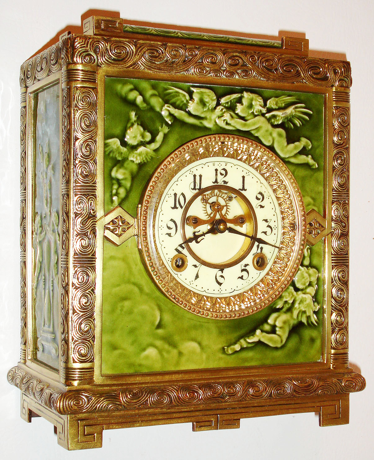 New Haven Clock Co., New Haven, Conn., "No. 1017" model, Asian influenced cast bronze case with green Aesthetic period Chelsea art tiles manufactured by J and G Low, Chelsea, Mass., the tiles depicting clouds, hovering and flying putti, and an hourglass, white enamel Arabic numeral dial, blued steel hands, cast bezel with beveled glass, 8 day, time and strike, movement with Brocot open escapement, c1885 — Antique Clocks Price Guide