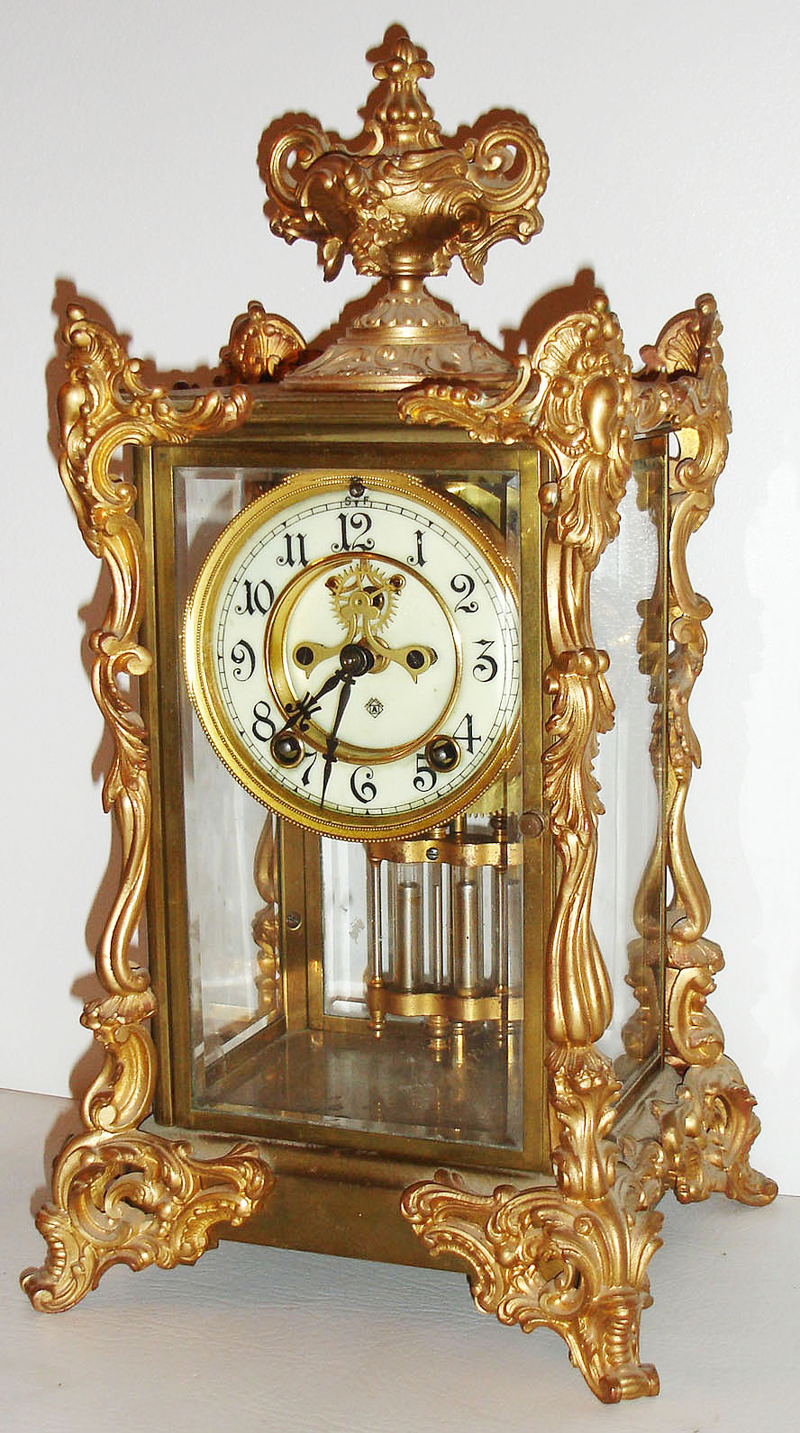 Ansonia Clock Co., Brooklyn, N.Y., "Marchionesse" model crystal regulator, polished brass case with ornate gilt ornament, beveled glasses, white enamel Arabic numeral dial, blued steel hands, 8 day, time and strike, movement with round plates, Brocot open escapement, gilt simulated mercury pendulum c1905 — Antique Clocks Price Guide