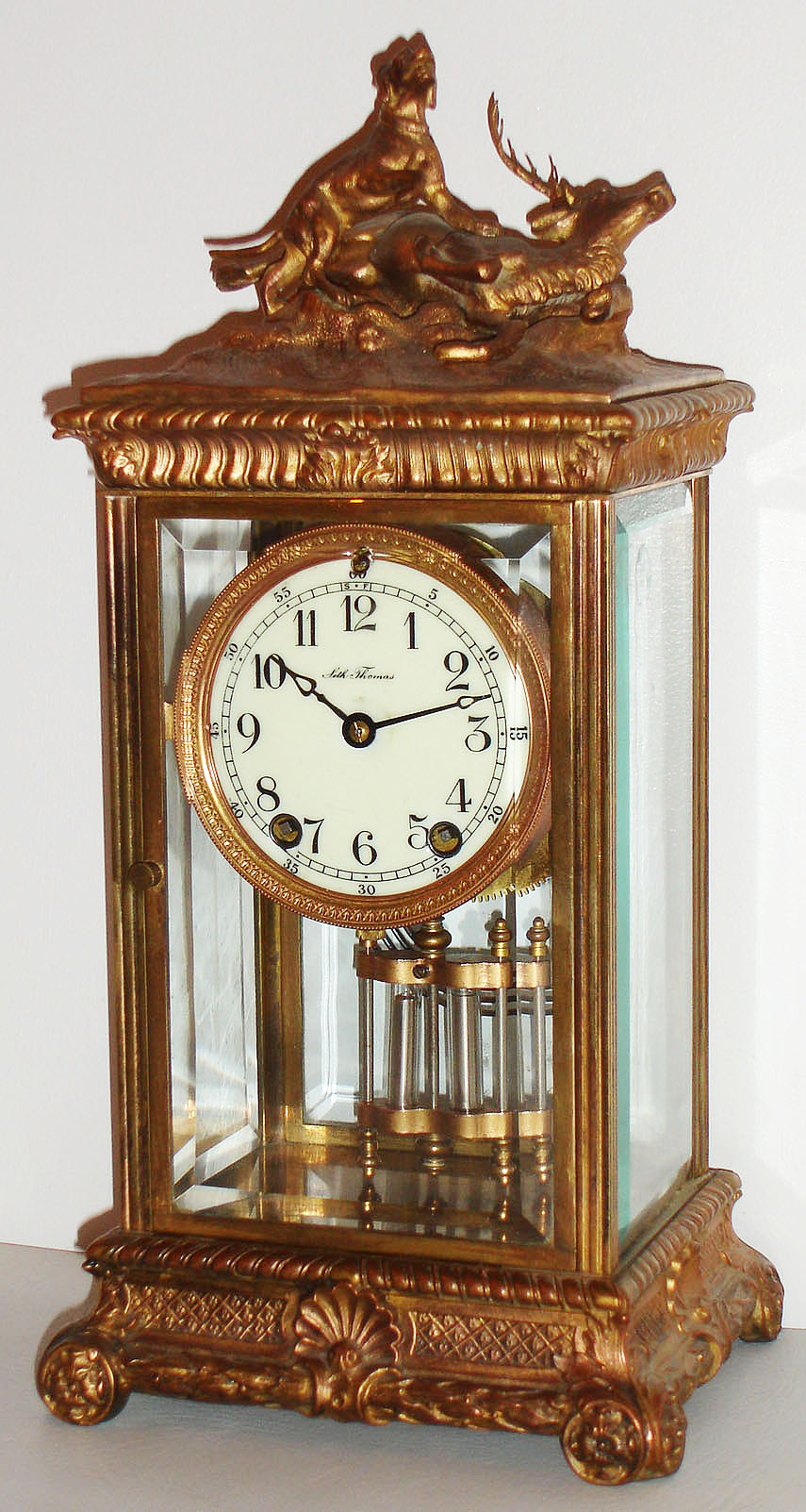 Seth Thomas Clock Co., Thomaston, Conn., "Empire No. 14" model crystal regulator, polished gilt case with gilt ornament, hunting scene at top, beveled glasses, white enamel Arabic numeral dial, blued steel hands, 8 day, time and strike, movement with round plates, gilt simulated mercury pendulum c1905 — Antique Clocks Price Guide