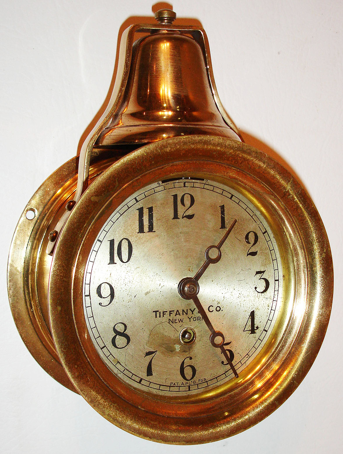 Boston Clock Co., for Tiffany and Co., N.Y., ships bell clock with 8 day tandem wind movement, both time and strike mainsprings wound by a single arbor, lever escapement, the front plate marked McMillans Pat., and numbered 98, silvered brass Arabic numeral dial marked "Tiffany and Co., New York", blued steel moon hands, heavy round brass case with lacquered surface, screw bezel, and bell mounted on top c1890 — Antique Clocks Price Guide
