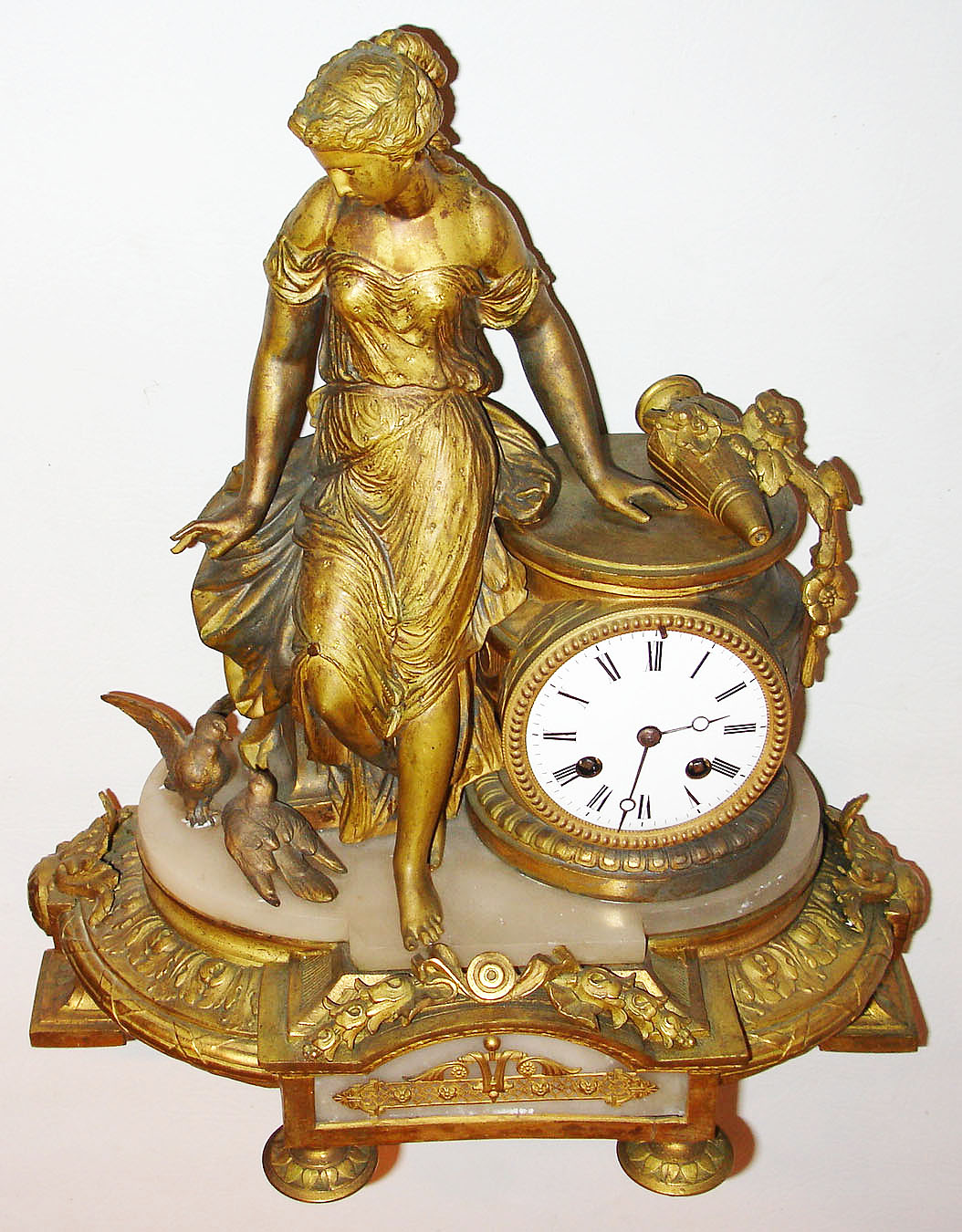 France, bright and matte gilt figural spelter and alabaster mantel clock, the female figure leaning against the clock case, and looking down at two birds, the base with acanthus, bellflower and fasces ornament, and an alabaster panel in the front with gilt ornament, white enamel Roman numeral dial with Breguet style hands, 8 day, time and strike, pendule a Paris movement, the case back signed "Ph. Mourey", c1870 — Antique Clocks Price Guide