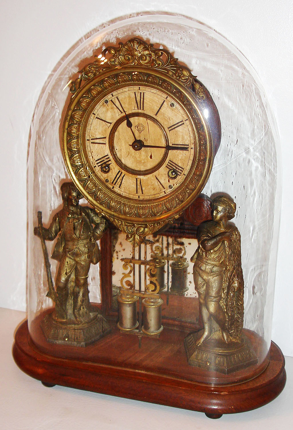 Ansonia Clock Co., New York, NY, "Crystal Palace No. 1 Extra", walnut base and back mounted with silvered figures of a fisherman and a hunter, flanking a central mirror, paper Roman numeral dial with blued steel hands, surrounded by a fancy lacquered cast brass bezel, eight day time and strike movement with Davies patent style pendulum, under a glass dome, c. 1880 — Antique Clocks Price Guide