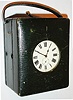 England?, leather bound travelling clock with Swiss thirty hour watch movement, pin pallet escapement, celluloid Roman numeral dial, backlit for viewing at night by depressing button on top of case, green velvet lining and key holder in front compartment, back compartment with battery holder, blued steel hands, c1910