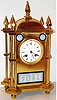 France, probably for the English market, a brass Gothic style mantel clock set with signed Wedgwood plaques, Japy Freres eight day time and strike movement, white enamel Roman numeral dial, Breguet style hands, bezel with beveled glass, polished brass case with columned corners, topped by acorn form finials, set with blue jasper plaques decorated with classical and allegorical motifs, each set in its own black painted, metal frame c1860