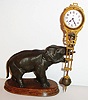 Junghans, Germany, "Elephant" model swinger, 8 day novelty timepiece, the patinated spelter elephant mounted to a molded beech wood base, his trunk supporting the gilt and patinated clock case/ pendulum, white enamel Arabic numeral dial, blued steel hands, ca.1920