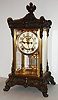 Ansonia Clock Co., Brooklyn, N.Y., "Elysian" model crystal regulator, ornate cast top and bottom with gilt finish, beveled glasses, white enamel Arabic numeral dial, 8 day, time and strike, movement with round plates, Brocot open escapement, gilt simulated mercury pendulum c1915
