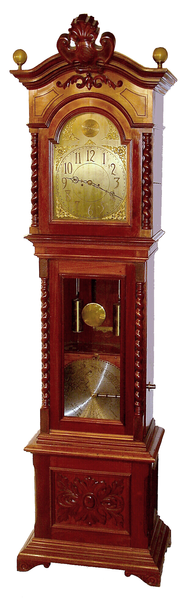 Regina Music Box Company, Rahway, NJ, "Regina No. 3 Hall Clock" tall clock with Regina music box, 8 days, time and strike, two brass weight driven movement by Seth Thomas Clock Co. in a mahogany case with barley twist columns flanking hood, shield type carved crest, spherical brass finials and applied carved base with a Regina double comb 15 1/2" disc music box set below pendulum in trunk exposed by glass door. The brass dial has corner spandrels and applied numerals, c1895 — Antique Clocks Price Guide