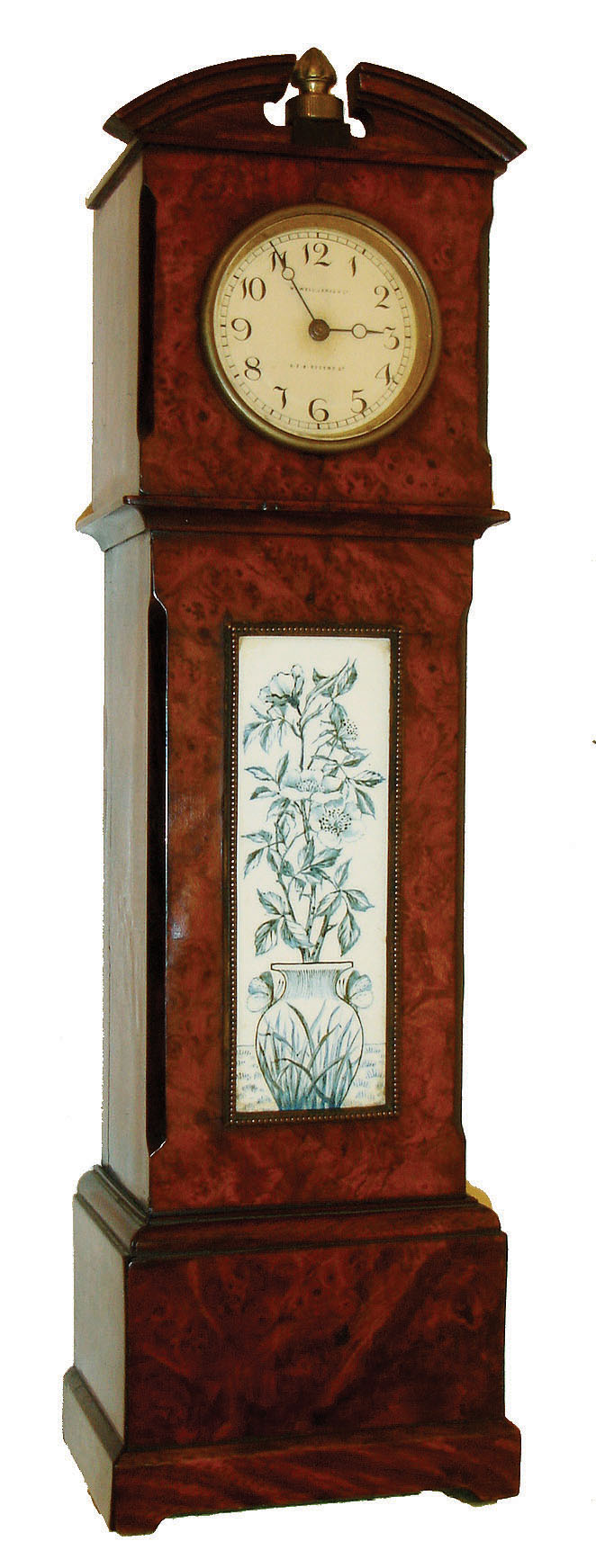Miniature tall clock, burl walnut veneered case, the trunk with brass framed ceramic panel decorated with a vase and flowers, Arabic numeral painted dial marked "Howell. James &amp; Co. 579 Regent St.", with Imhof 8 day timepiece movement, the clock finial serving as winding crown, c 1910 — Antique Clocks Price Guide
