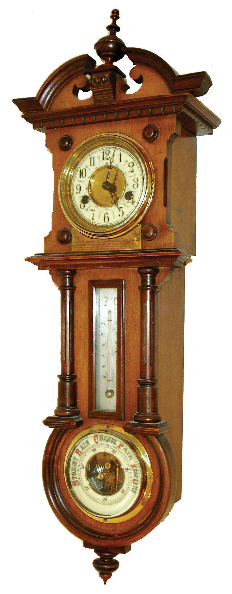 Hamburg American Clock. Co., Germany, small 8 days, time and strike, wall clock with barometer and thermometer, walnut case with molded cornice and mid section, door of inverted keyhole shape and containing a thermometer and aneroid barometer, the barometer with colorful enamel dial, thermometer with silvered scale, removable case top with broken arch and plinth with finial, case bottom also with drop, brass bezel with beveled glass, Arabic numeral white enamel dial, blued steel hands, engraved plaque with dedication below dial, c1895 — Antique Clocks Price Guide