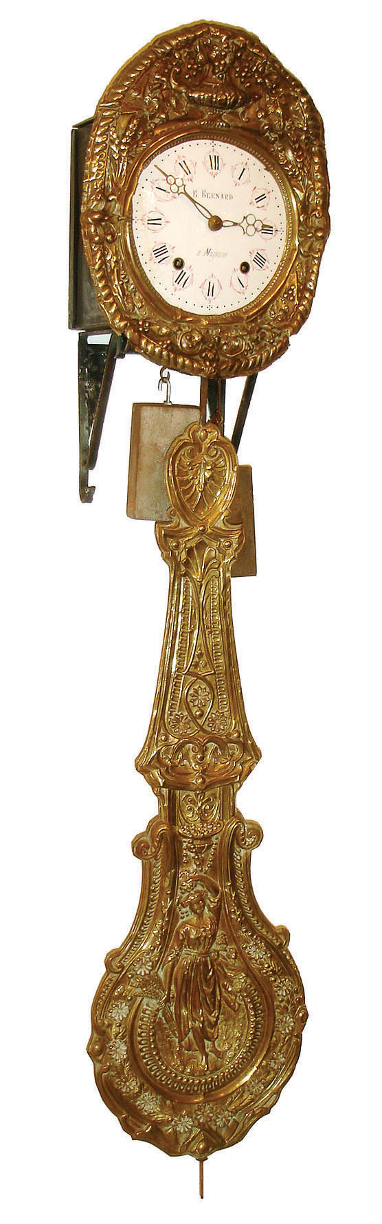 France, Morbier clock, 8 days, time and strike, with brass dial surround with urn, flowers, wheat and grapes and gadrooned edge, Roman numeral white enamel dial, signed "E. Bernard a Mayenne", pierced brass hands, Rectangular cast iron weights, stamped brass pendulum featuring a female figure with harvest bounty, with iron wall bracket, late 19th century — Antique Clocks Price Guide