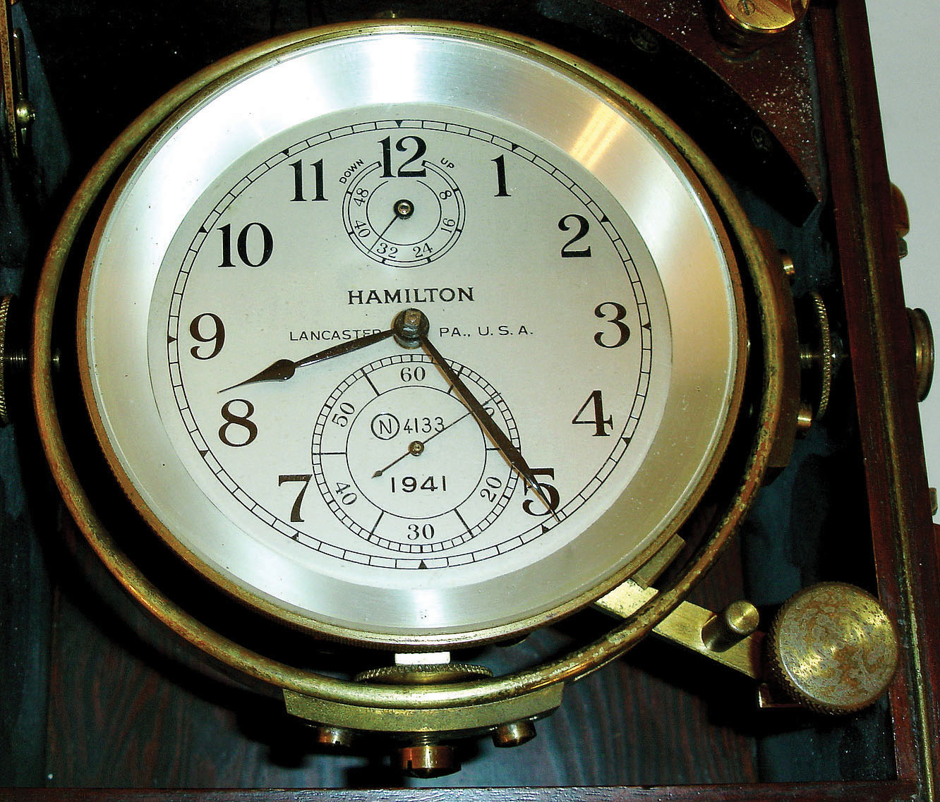 Hamilton Watch Co., Lancaster, Penn., model 21 marine chronometer, 14 jewel key wind and set, straight line damascened nickel plate movement, with spring detent escapement and chronometer balance with helical hairspring, in a gimbaled brass bowl with screw bezel, and Arabic numeral, metal dial with wind indicator, black painted steel spade and poker hands, contained in mahogany inner and outer boxes with brass hardware, serial #2E4133, c1941 — Antique Clocks Price Guide
