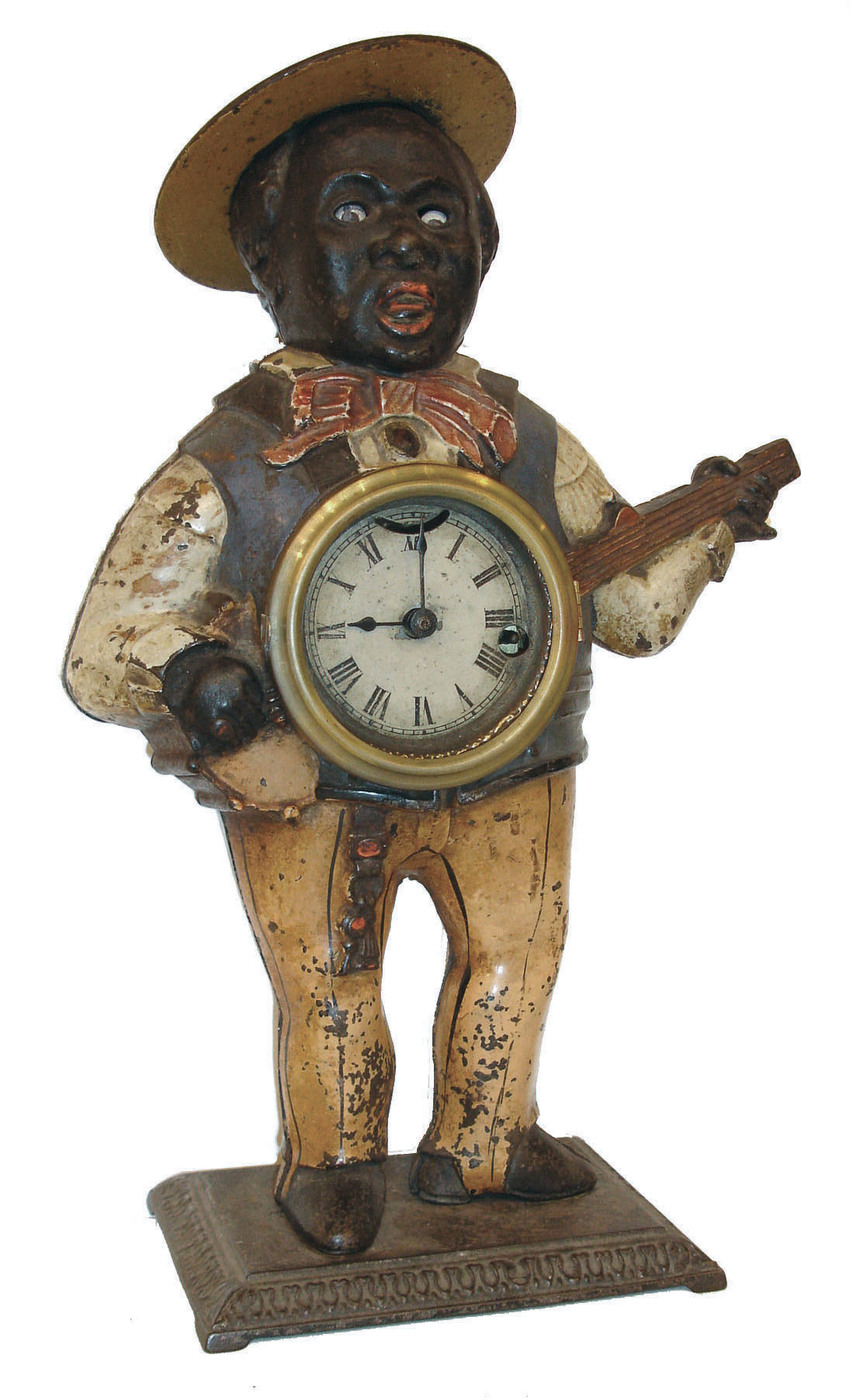 Waterbury Clock Co., "Sambo" blinking eye novelty clock, the figure in brightly colored clothing and playing a banjo, with clock mounted in his belly, Roman numeral painted dial, 30 hour lever timepiece, with linkage to escapement for blinking eyes, all on a molded cast iron base, c1860 — Antique Clocks Price Guide