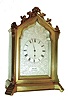 Dent, London, 8 day time only, desk clock in the Gothic style, the gilt case with stepped base and molded feet, gable with applied scroll ornament, modified lancet arch front with conforming, silvered dial mask framing a foliate engraved silvered Roman numeral dial, the center with engine turning, and signed "Dent London" below the chapter ring, blued steel spade and poker hands, small French style carriage timepiece movement with lever platform, case back with apertures for regulation, setting and winding, with shutter for exclusion of dust, and marked "3038", stamped crown over a lozenge shaped reserve marked "E.W.S.", an hourglass, and banner with "Machine Made", c1870