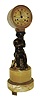 France, figural mantel clock, round siena marble base, gilt feet with foliate ornament, patinated putto with arms crossed, seated on a stump and with tambourine and pipes at his feet, the drum form clock case balanced on a wreath atop his head, Roman numeral gilt metal dial with engine turned center, 8 days, time and strike, pendule a Paris movement marked "Canchy", pinwheel escapement with escape wheel and pallets planted outside back plate, silk suspension, c1840
