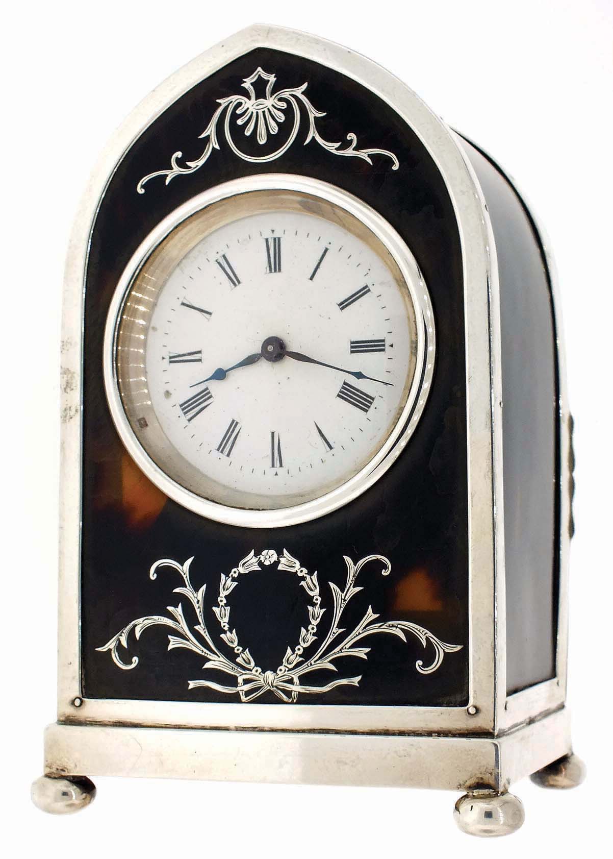 England, lancet arch-shaped desk clock, silver gilt frame on compressed ball feet, with London hallmark and date letter for 1907. The front and sides have tortoise shell panels and engraved silver inlay, Roman numeral white enamel dial, blued steel hands, French, 8 days, timepiece movement with lever platform — Antique Clocks Price Guide