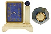 Clocks- 2 (Two): An Art Deco style desk clock with alabaster case and lapis lazuli dial marked ÓGubelin LucerneÒ, and a trapezohedronal confusionite (possibly also lapis), paperweight clock mounted with an 18 karat yellow gold Accutron calibre 214 timepiece, the dial and case signed Tiffany & Co.