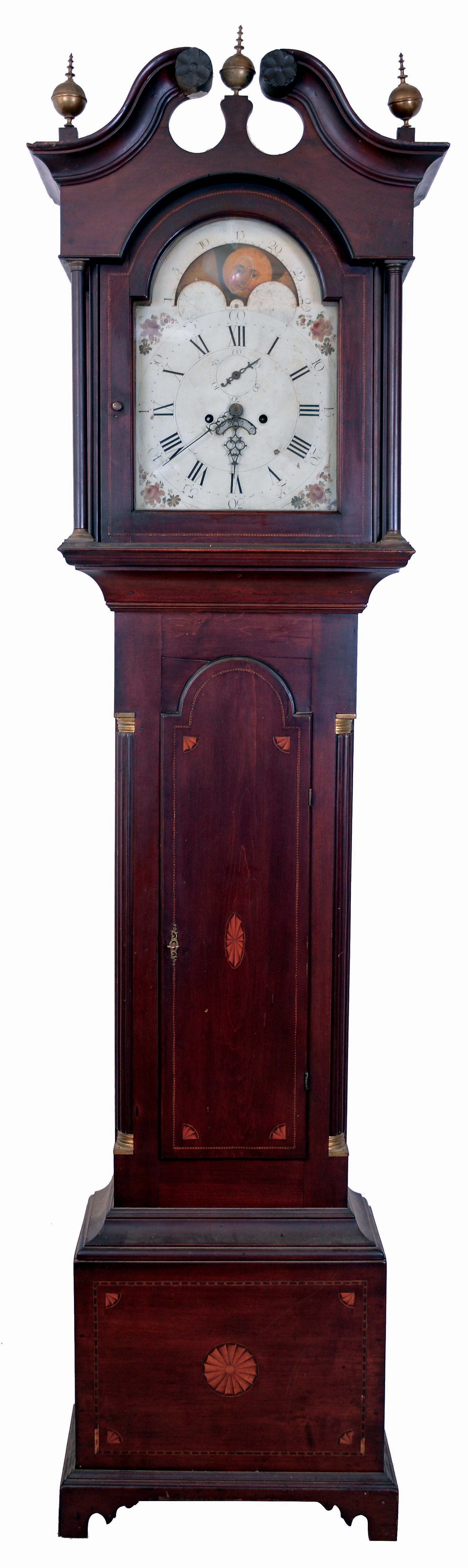 American tall clock, 8 days, time and strike, weight driven brass movement in an inlaid cherry case with broken arch top with carved rosettes, hollow carved corner columns and brass capitals, inlaid trunk with corner and center fans and inlaid plinth with corner and center fans and bell flower banding. Painted white dial with moon phase and calendar, c1810 — Antique Clocks Price Guide