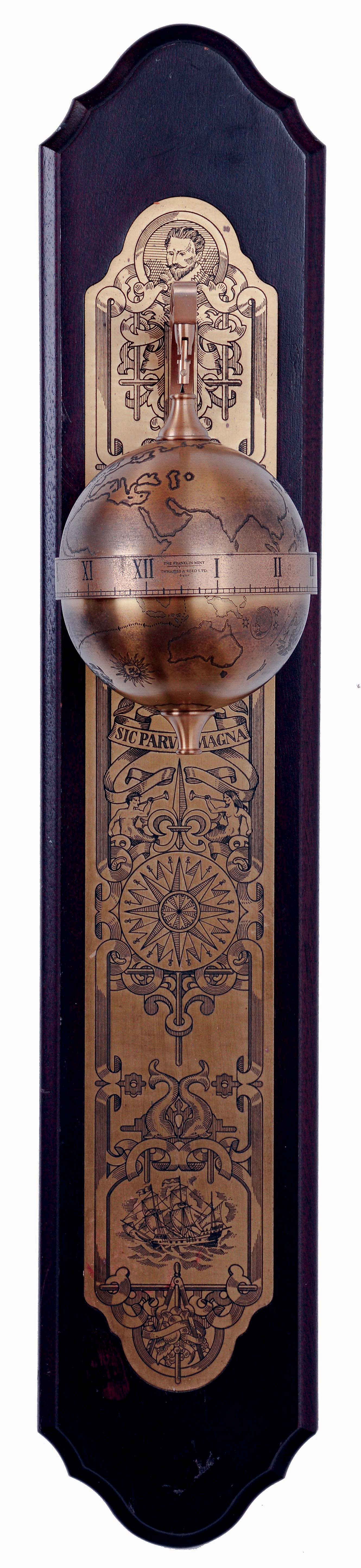 Thwaites &amp; Reed, England for the Franklin Mint, Sir Francis Drake model falling ball gravity clock. The spherical, weighted, engraved brass case containing the 8 day timepiece movement, and with annular time display, suspended from a bracket affixed to a wall mounted board, with engraved ornamental brass back plate, c1980 — Antique Clocks Price Guide
