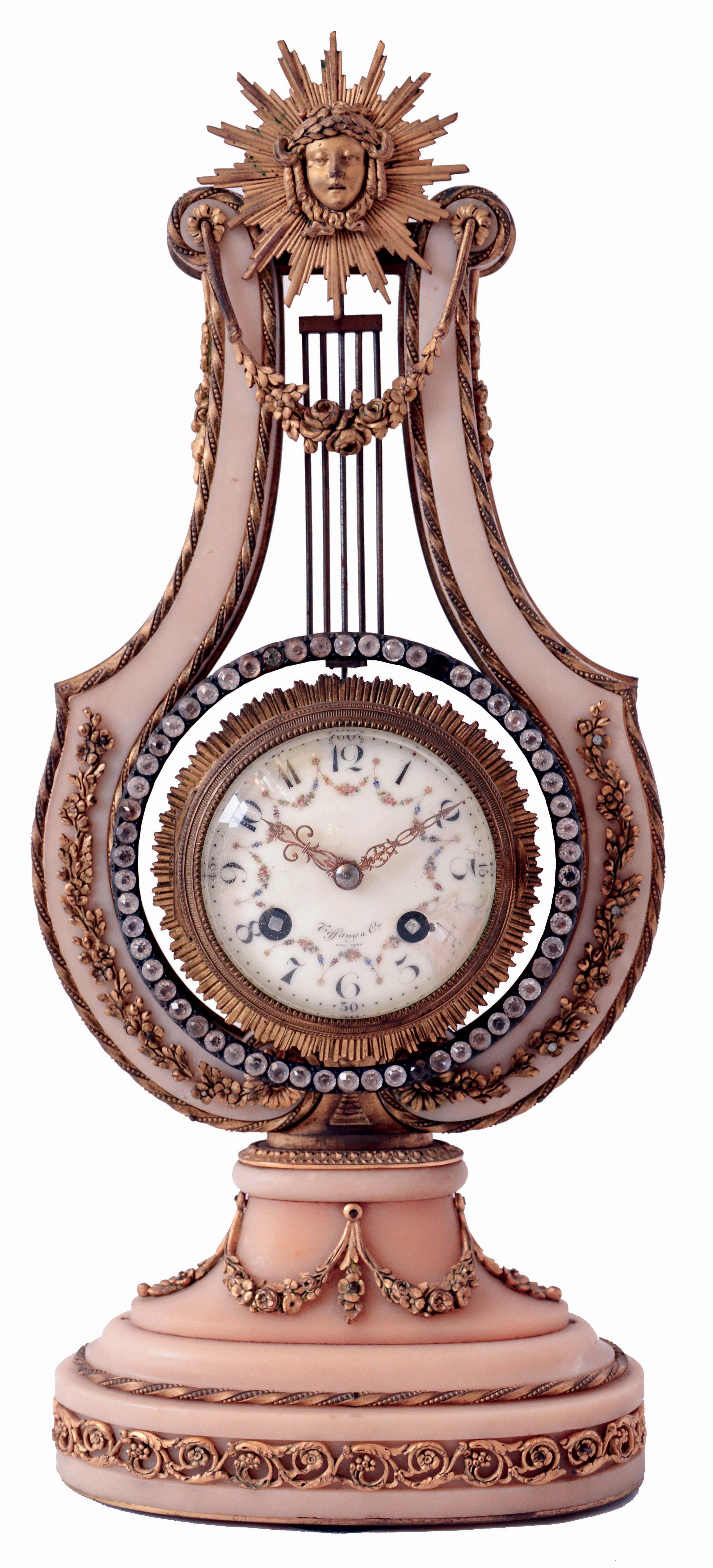 France, for Tiffany &amp; Co., New York, lyre form mantel clock, white marble case decorated with gilt bronze ornament including floral festoons and other foliate ornament, the top with Helios mask, the pendulum suspended behind mask and with oscillating ring of brilliants, Arabic numeral white enamel dial, 8 days, time and strike pendule a Paris movement, dial and movement signed, c1900 — Antique Clocks Price Guide
