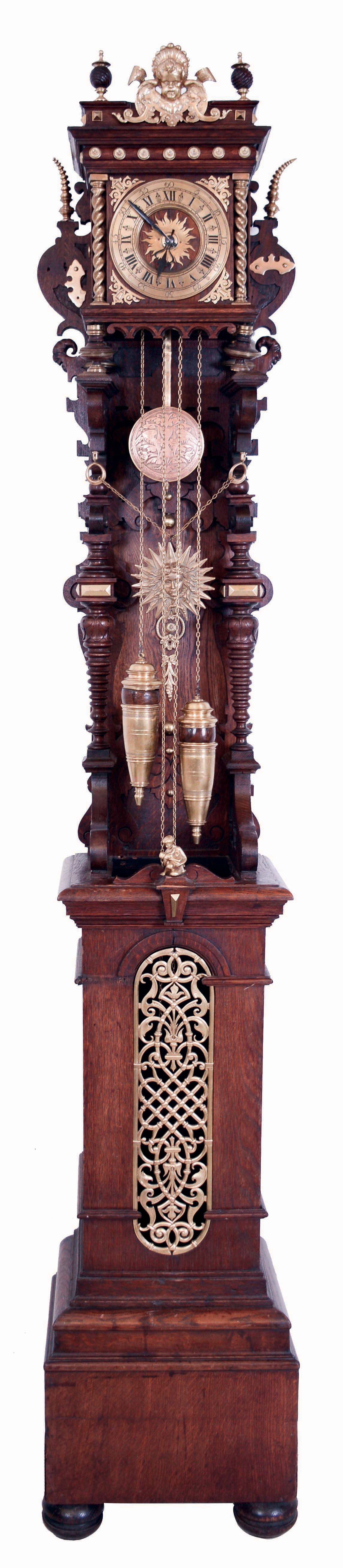 RSM, Germany, open well tall clock, 8 days, time and strike, brass weight driven movement in a well carved walnut case with columns supporting hood, bun feet, matching pendulum and weight decoration, silvered brass dial, c1910 — Antique Clocks Price Guide
