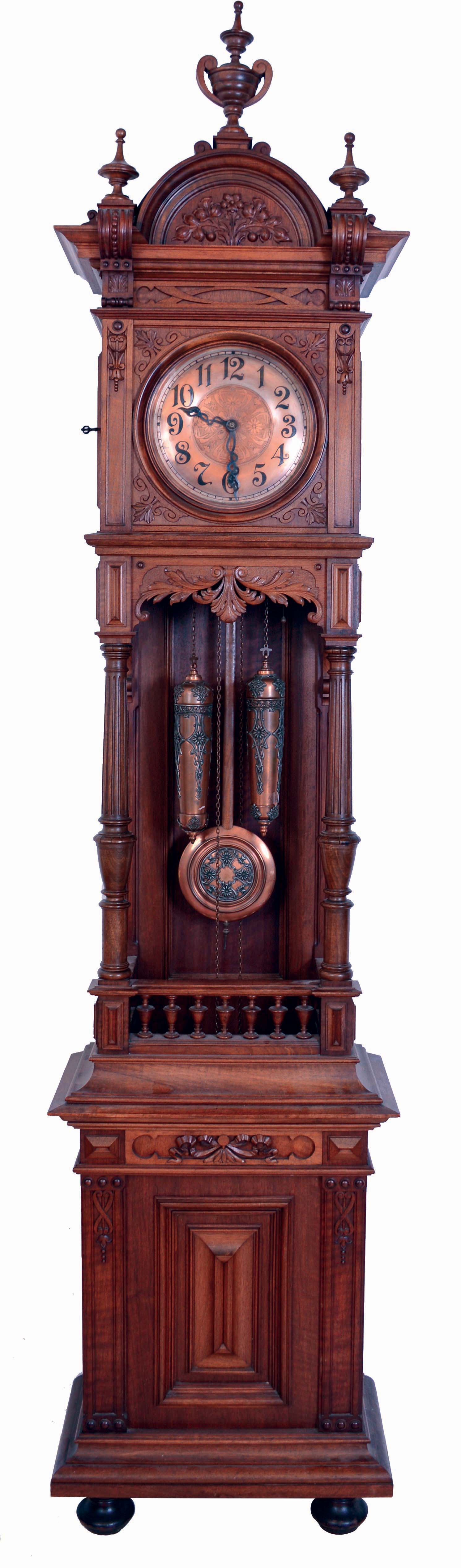 Furtwangler, L. &amp; Sohne, Furtwangen, Germany, open well tall clock, 8 days, time and strike, on gong, brass weight driven movement in a carved walnut case on bun feet with large turned finials and copper finished brass dial. The dial, pendulum bob and weights are matching filigreed copper tone, serial #13235 — Antique Clocks Price Guide