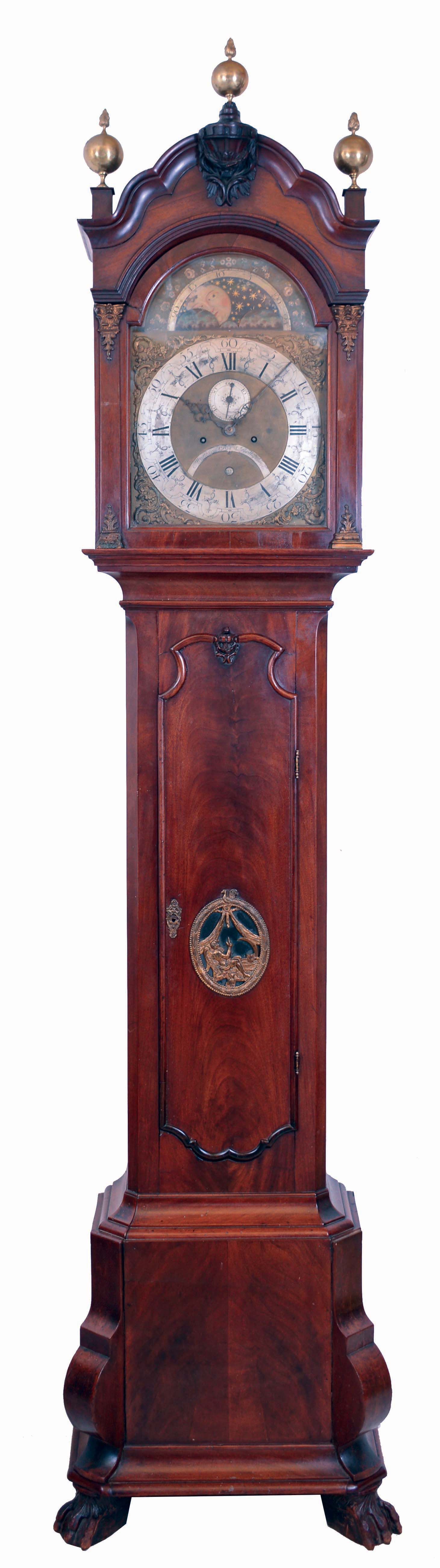 Matthijs Bras, Rotterdam, Netherlands, tall clock, 8 days, time and Dutch bell strike, weight driven movement in a mahogany case with crotch mahogany door and base, brass cartouche revealing pendulum, paw feet, scalloped arched hood with carved center element and brass capitals on columns flanking hood and cast brass finials. The brass dial has a silvered chapter ring, cast brass spandrels, moon phase, half boss with maker's signature, circa late 18th century — Antique Clocks Price Guide