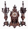 France, three piece mantel garniture showing renaissance revival influence, the bronze clock case with gadrooned base on scroll feet, openwork center section with central caryatid, foliate ornament, and pilasters, the case top with lion mask, finials, and surmounted by a gadrooned urn, brass repousse dial with Roman numeral, white enamel cartouches, 8 days, time and strike movement with Helios mask pendulum, with a pair of candelabra matching the clock, c1880