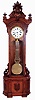 Wm. L. Gilbert Clock Co., Winsted, Conn., "Regulator No. 7", floor standing jeweler's regulator, 8 days, time only, brass weight driven Swiss pinwheel movement with a white enameled dial, lyre gridiron pendulum in a walnut case with burled highlights and intricately carved crest with busty lady figure, c1881