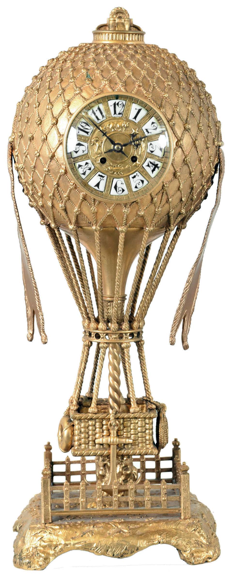 France, table clock, gilt bronze hot air balloon form case with suspended gondola, laden with sand bags, anchor, ring, and rope, resting on a stump surrounded by a fence, all on a cast base with foliate ornament, gilt dial set with Arabic numeral white enamel cartouches, the center with four signs of the zodiac, fancy blued steel hands, 8 day, time and strike pendule a Paris movement, the back plate with Japy Freres medallion within an engraved heart — Antique Clocks Price Guide
