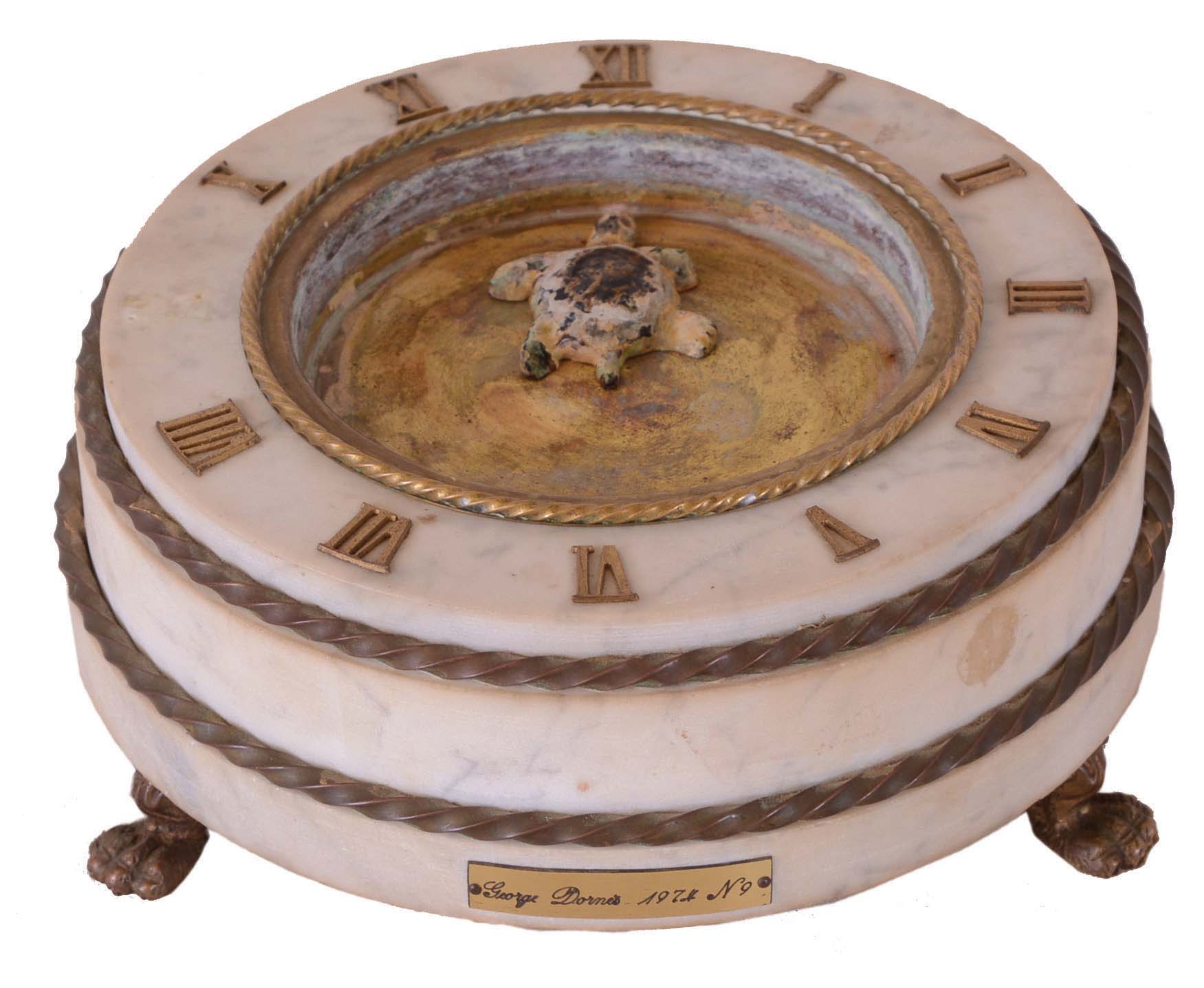 George Dorne, Turtle mystery clock, round, white marble basin with brass trim and reservoir, applied Roman numerals, and resting on cast brass paw feet, quartz movement, the turtle pointing to the time and controlled by a magnet attached to the movement — Antique Clocks Price Guide