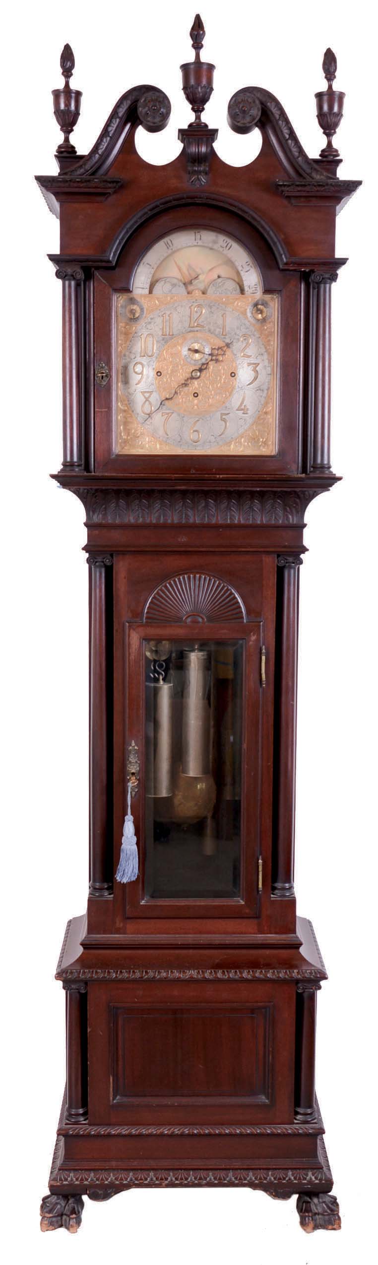 Walter H. Durfee, Providence, Rhode Island, 9 tube hall clock, 8 day, time, strike and quarter chimes, triple weight driven movement playing Westminster or Whittington chimes on tubes which are signed Walter Durfee with the patent date 1887. The brass dial signed Durfee has a silvered chapter ring with pierced brass spandrels and dial center, moon phase depicting sailing scene, strike / silent and tune selector dials. The case is mahogany and has carved cornice moldings, carved paw feet, carved broken arch top with flame finials and four full columns flanking hood, sunburst carving above trunk door flanked by four full columns and beveled glass in hood and trunk doors and raised panel on base. There are exceptional lion's head escutcheons on both hood and trunk doors. — Antique Clocks Price Guide